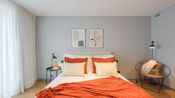 Una cama bien hecha con un edredón rojo, dos almohadas y una mesita de noche con una lámpara. Encima de la cama, hay dos cuadros enmarcados en la pared.