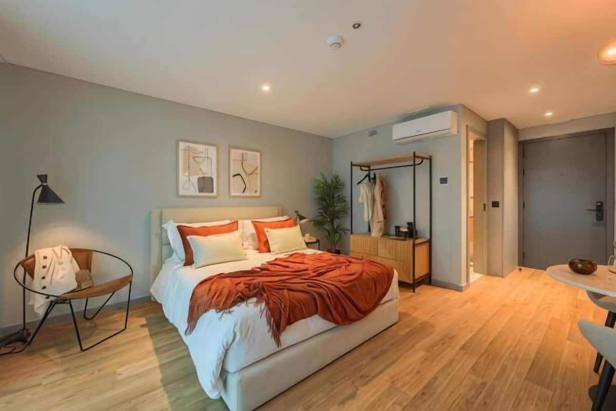 Un dormitorio moderno con cama, mesita de noche, lámpara y una planta.