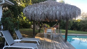 Um deck de madeira com espreguiçadeiras, uma mesa e uma rede.