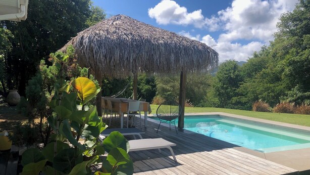 Um deck de madeira com piscina, um guarda-sol de palha e uma área de estar.