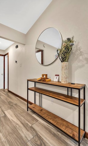 Un couloir avec une console en bois, un miroir rond, un vase avec des plantes et un banc en bois.