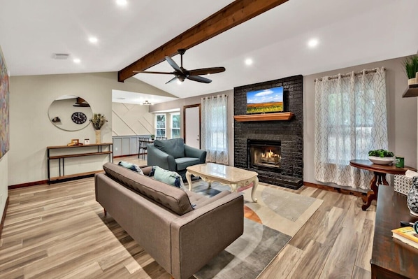 Un salon moderne avec une cheminée, un ventilateur de plafond et un coin repas à l’arrière-plan.