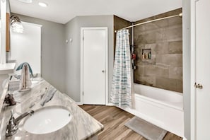 Une salle de bain avec un lavabo en marbre, une douche avec un rideau à rayures et une porte donnant sur une autre pièce.