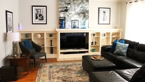 Una sala de estar con televisor, sofá, sillón, mesa de centro y alfombra estampada.
