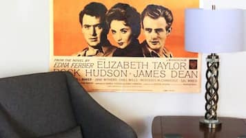 Un cartel de película en una pared, un sillón oscuro y una mesita de madera con una lámpara.