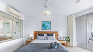 Una camera d'hotel con un letto, comodini, una finestra con vista e una porta scorrevole in vetro che dà su un balcone.