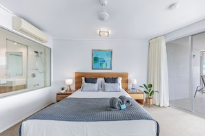 A hotel room with a bed, bedside tables, a nightstand, a window with a view, and a sliding glass door leading to a balcony. - Nature's Window On Airlie (Airlie Beach)