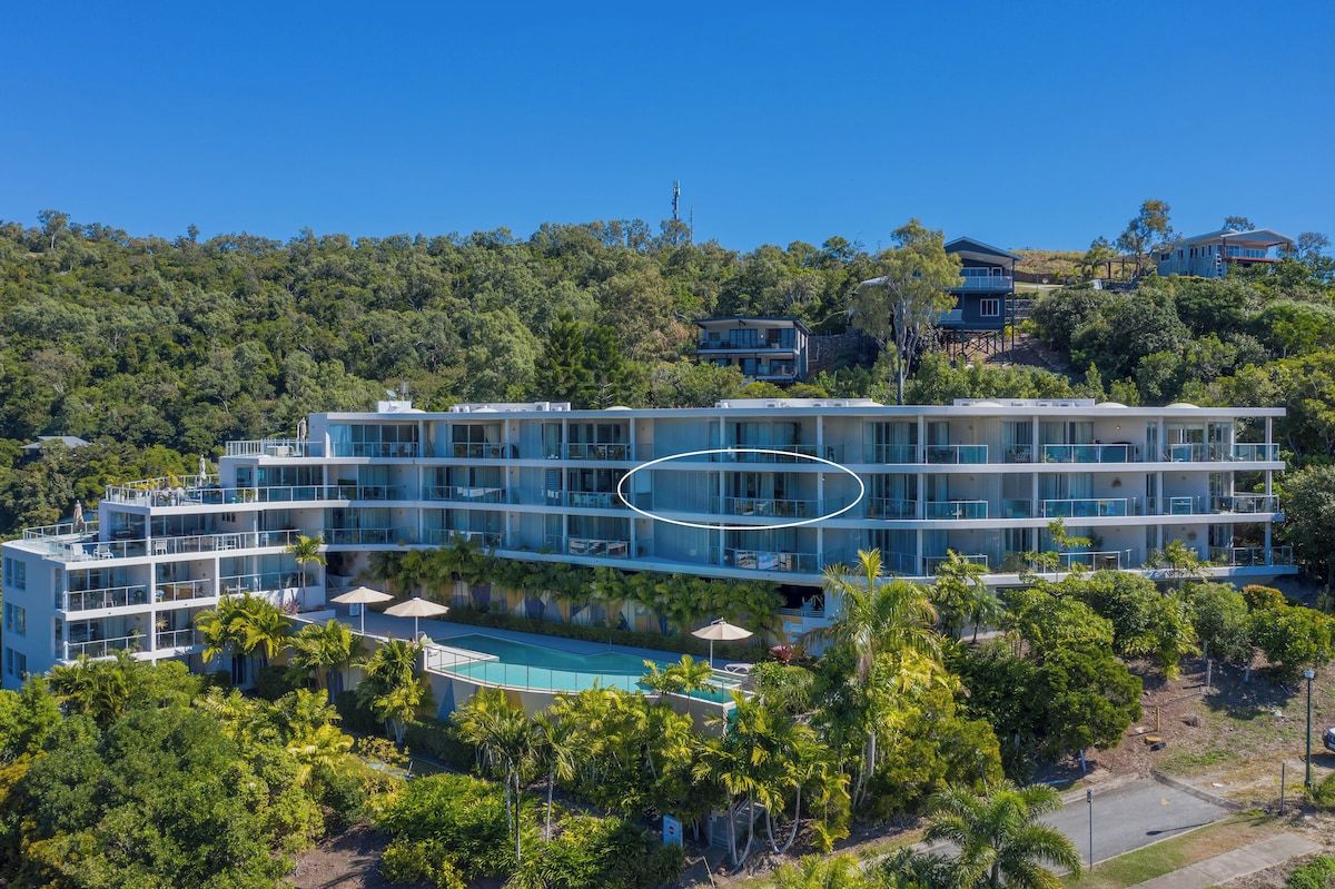 A multi-story hotel with a pool, surrounded by greenery and hills.