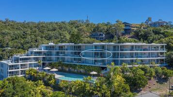 A multi-story hotel with a pool, surrounded by greenery and hills.