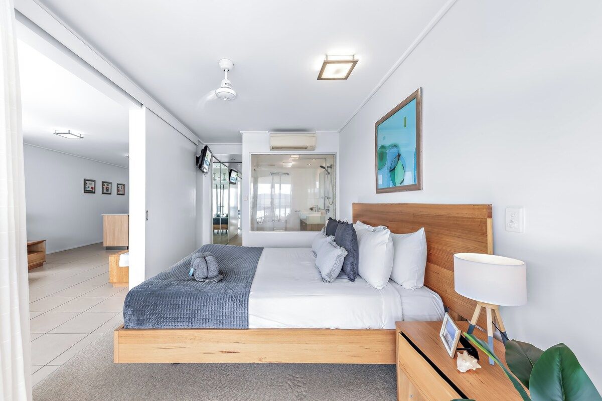 Un dormitorio moderno con una cama de madera, una mesita de noche con lámpara y un ventanal grande.