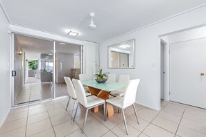 Un espace repas moderne avec une table en verre, des chaises blanches et une plante en pot.
