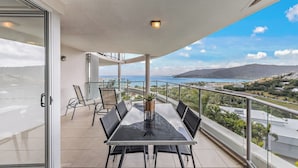 Un balcone con una porta vetrata, un tavolo con sedie e vista sul mare e sulle colline.