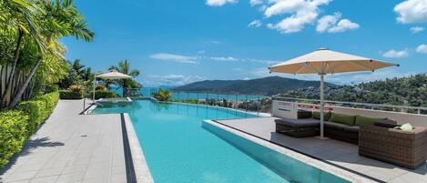 Une piscine avec vue sur la mer et les montagnes, entourée de chaises longues et de parasols.