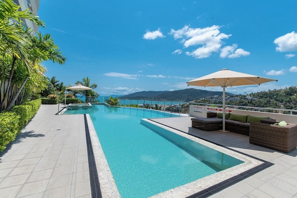 Ein Swimmingpool mit Blick auf das Meer und die Berge, umgeben von Liegestühlen und Sonnenschirmen.