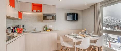 A modern kitchen with a dining area, a flat-screen TV, and a large window with a snowy view.