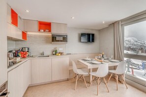 A modern kitchen with a dining area, a TV mounted on the wall, and a view of a snowy landscape through large windows. - 10m from resort center, 4th floor, view mountain, tv, ski locker, 40m², Tignes (Tignes)