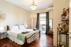 Une chambre avec un lit en bois, un lustre, un balcon avec vue et une étagère remplie de peluches.