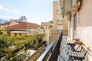 Un balcon avec une table et des chaises, donnant sur un quartier résidentiel avec des immeubles et des arbres.