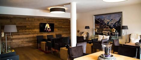 A modern interior with a wooden wall, a fireplace, and a dining area with chairs and tables.