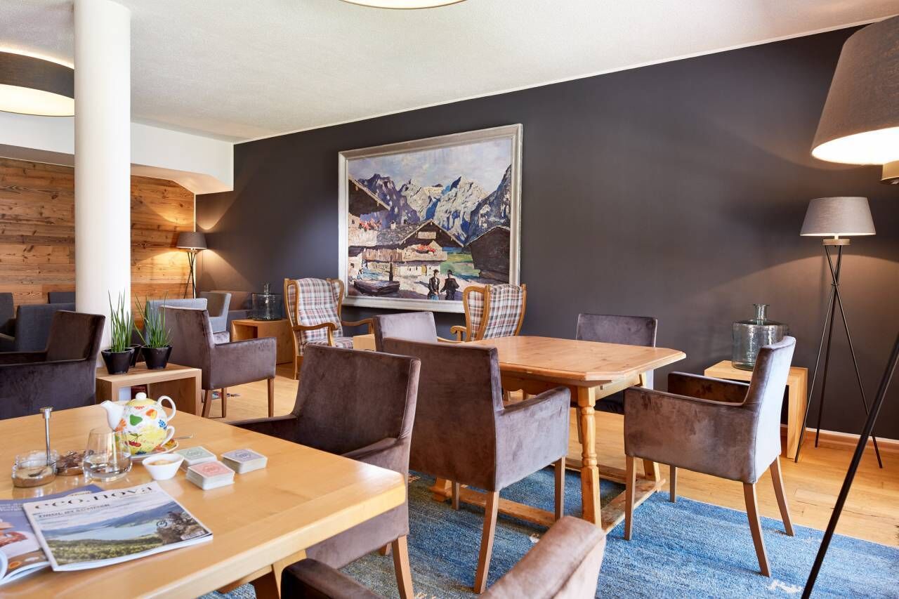 Een moderne hotelkamer met een houten eettafel, zachte zitplaatsen, een groot schilderij aan de muur en een vloerlamp.