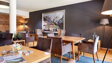 Een moderne hotelkamer met een houten eettafel, zachte zitplaatsen, een groot schilderij aan de muur en een vloerlamp.