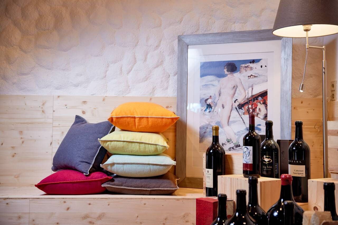 Un banco de madera con cojines coloridos, un cuadro enmarco y botellas de vino.