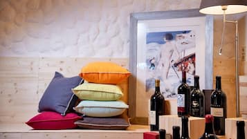 Un banco de madera con cojines coloridos, un cuadro enmarco y botellas de vino.