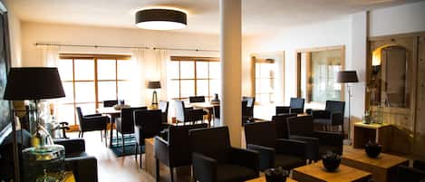 A modern hotel lobby with a central seating area, multiple tables, and chairs.