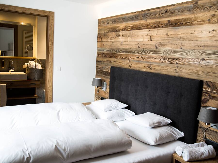 Una camera da letto con un letto grande, una testiera in legno, un comodino con una lampada e un bagno con lavandino e porta asciugamani.