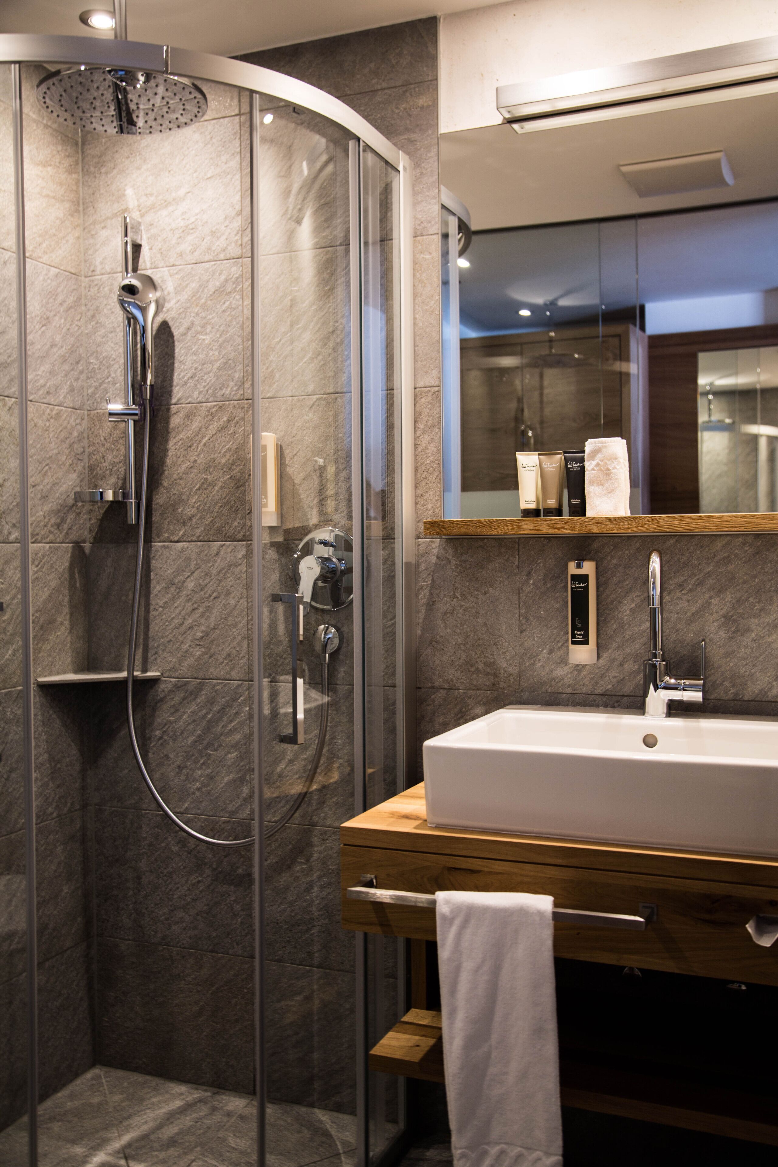 Un baño moderno con ducha de vidrio, tocador de madera con lavamanos blanco y un espejo sobre el tocador.