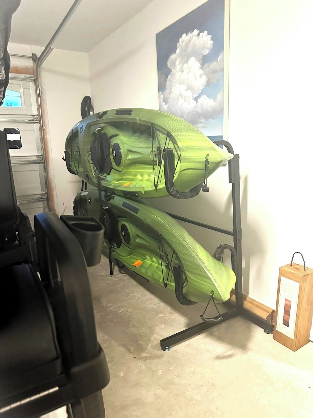 Un kayak est posé sur un support dans un garage dont le sol est en béton et dont un des murs est décoré d’une peinture représentant des nuages.