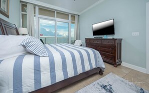 A bedroom with a large bed, a dresser, a television, and a balcony with a view. - Phoenix Gulf Shores 1602-1 1 Bedroom Condo (Gulf Shores)