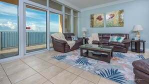A living room with two brown leather sofas, a glass coffee table, and a floral rug. There are two lamps on side tables and two paintings on the wall. - Phoenix Gulf Shores 1602-1 1 Bedroom Condo (Gulf Shores)