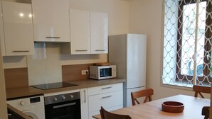 Une cuisine moderne avec des meubles blancs, un four à micro-ondes, un lave-vaisselle et un coin repas comprenant une table et des chaises en bois.