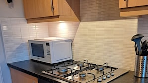 Eine moderne Küche mit Holzschränken, einem Gasherd, einer Mikrowelle und einem Edelstahl-Küchenhelferhalter.