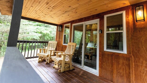 A wooden deck with two wooden chairs and a glass door leading to a room.