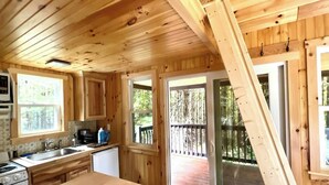 A wooden cabin kitchen with a large window, a sink, a stove, and a door leading to a deck.