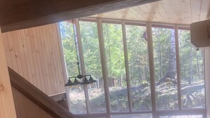 A wooden staircase leading to a large window with a view of a forest. - Adirondack Home on Lake Snow (Indian Lake)