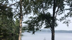 A lakeside deck with a wooden platform, surrounded by trees and a grassy area. - Adirondack Home on Lake Snow (Indian Lake)