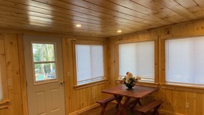 A wooden-paneled room with a wooden table and benches, a door, and windows with blinds. - Adirondack Home on Lake Snow (Indian Lake)