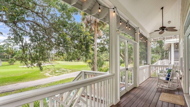 Un portico coperto con vista su un campo da golf, ringhiere in legno e una ventola a soffitto.
