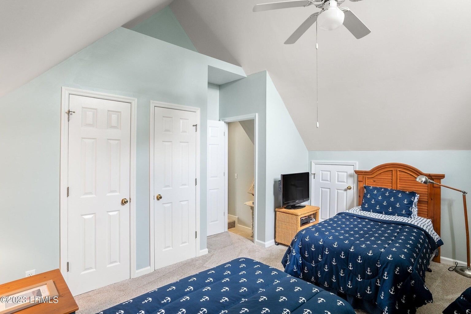 Une chambre avec deux lits, un ventilateur de plafond et un téléviseur posé sur une petite table.