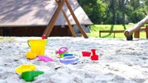 A sandy area with beach toys and a wooden structure in the background. - Gemütlicher Bungalow in Storkow am See (Storkow)