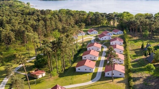A cluster of white houses with red roofs, surrounded by dense forest and a lake in the background. - Gemütlicher Bungalow in Storkow am See (Storkow)