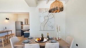 A modern dining area with a wooden table, white upholstered chairs, and a decorative wall piece. - Above Blu Villa - Two Bedroom Villa, Sleeps 4 (Gaios)