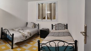 Un dormitorio pequeño con dos camas individuales, un armario, una ventana con cortinas y un suelo de cuadros.