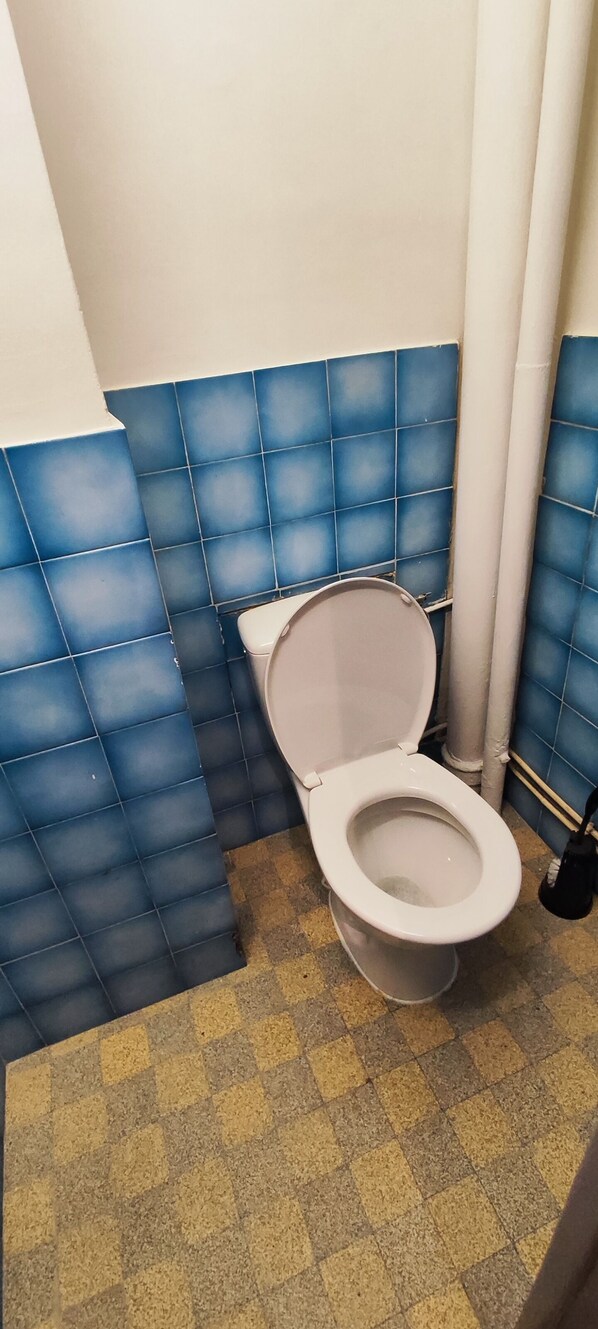 A toilet with a white seat and lid, blue tiled walls, and a yellow checkered floor.