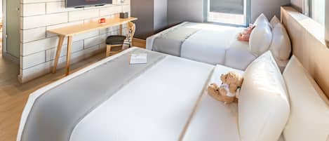 A hotel room with two beds, a desk, a TV, and a window.