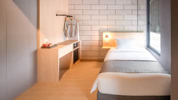 A compact hotel room with a bed, bedside table, and a small desk with a chair.
