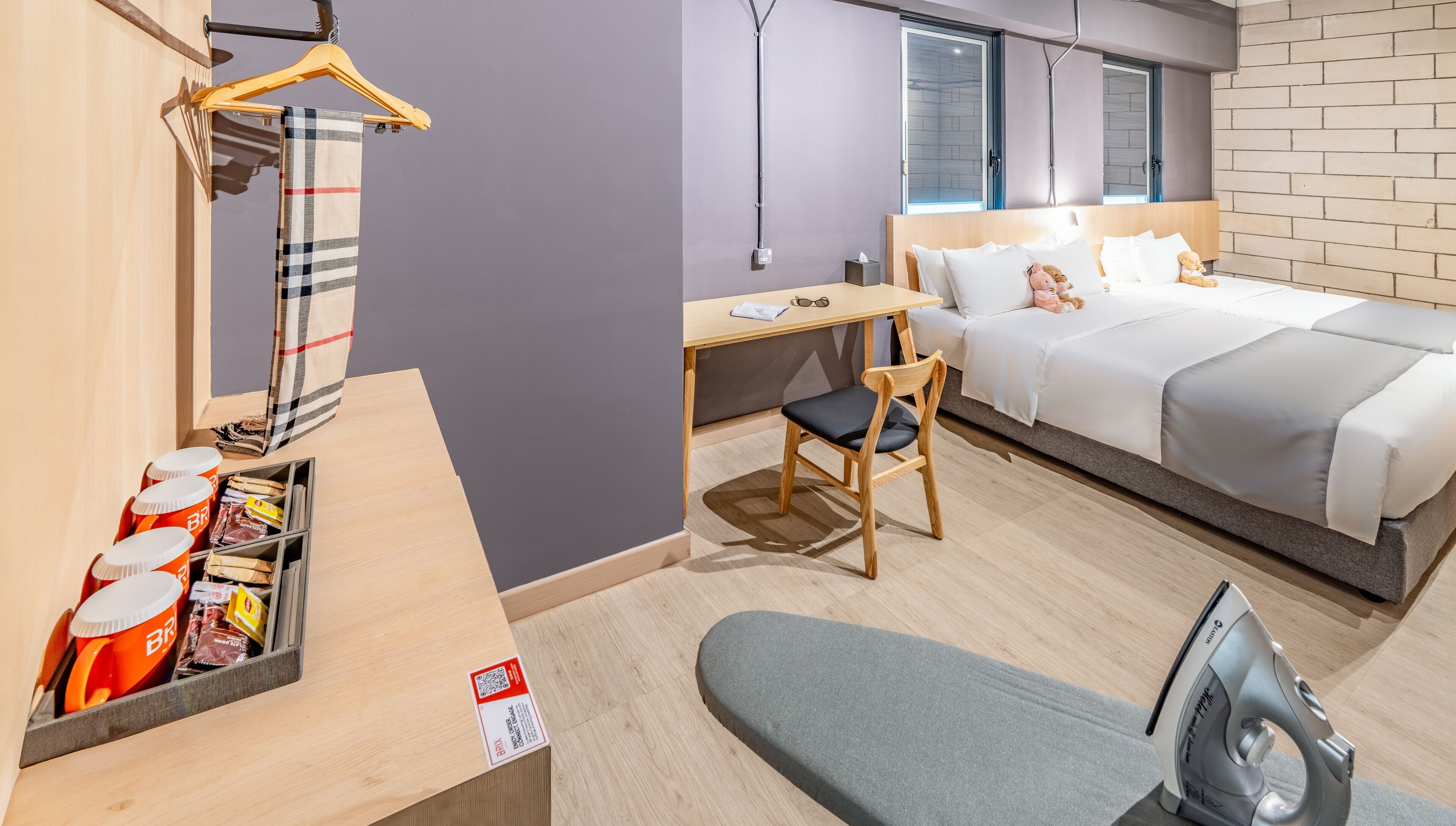 A modern hotel room with a bed, a desk, a chair, and a hanging light fixture.
